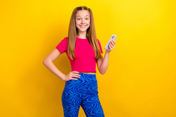 照片正面可爱漂亮的女学生直发，穿着粉红色的t恤，拿着智能手机孤立在黄色背景图片下载