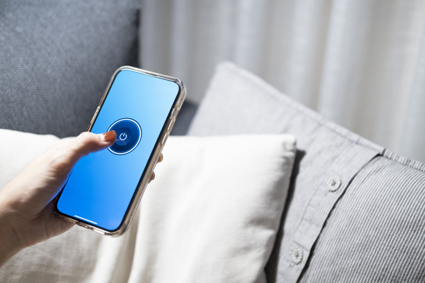 智能家居概念通过移动应用程序控制灯光、灯具或家用电器。女人的手是通过她在床上或沙发上的手机关掉灯图片下载