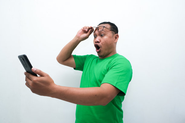 照片中，一名亚洲男子看着手中的手机，露出震惊的表情图片下载