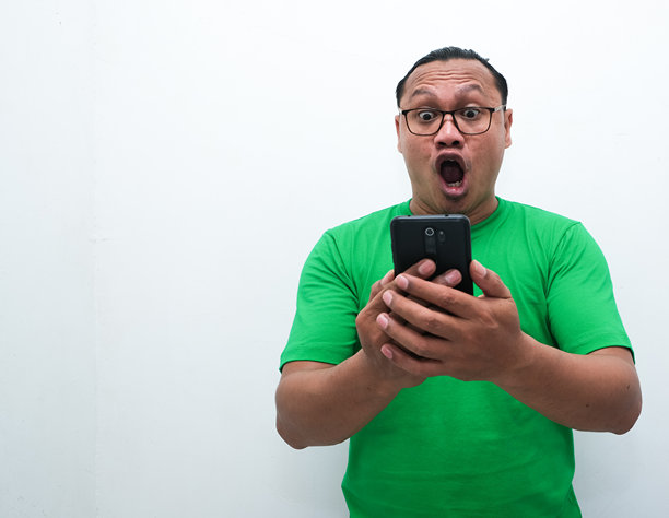 照片中，一名亚洲男子看着手中的手机，露出震惊的表情图片下载