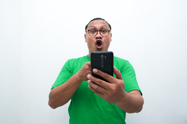 照片中，一名亚洲男子看着手中的手机，露出震惊的表情图片下载