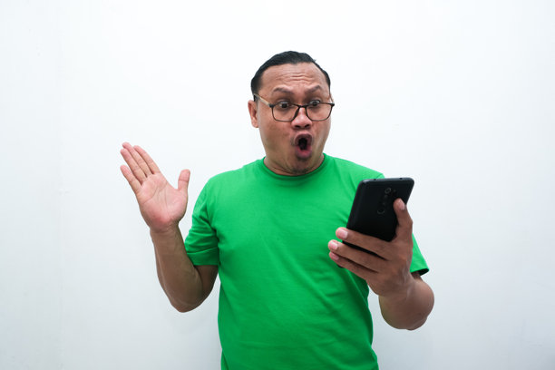 照片中，一名亚洲男子看着手中的手机，露出震惊的表情图片下载