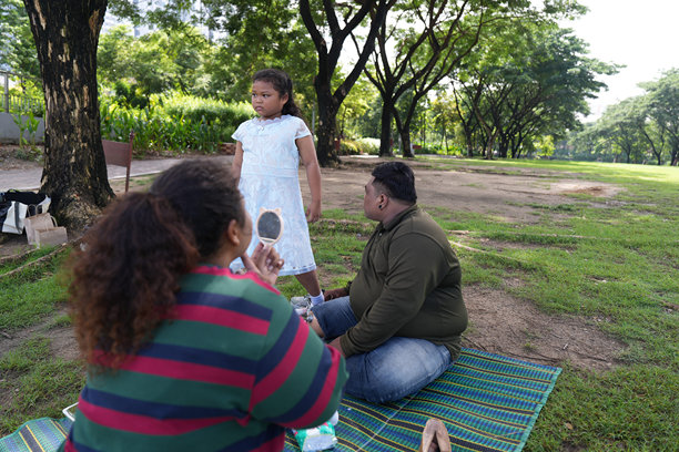 一个又大又胖的亚洲家庭，爸爸、妈妈、女儿在公园里野餐，他们坐着吃零食。他们坐着做作业，互相送花。他们很开心。图片下载