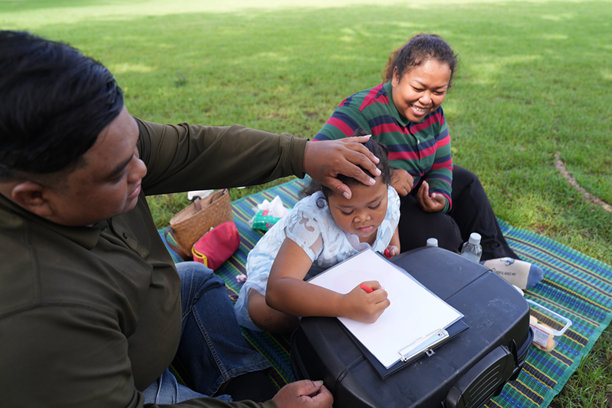一个又大又胖的亚洲家庭，爸爸、妈妈、女儿在公园里野餐，他们坐着吃零食。他们坐着做作业，互相送花。他们很开心。图片下载