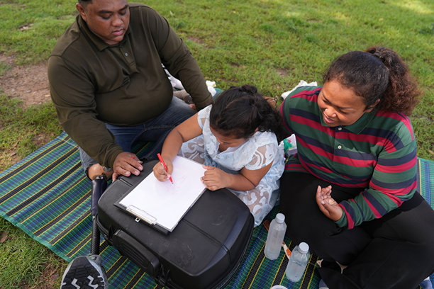 一个又大又胖的亚洲家庭，爸爸、妈妈、女儿在公园里野餐，他们坐着吃零食。他们坐着做作业，互相送花。他们很开心。图片下载