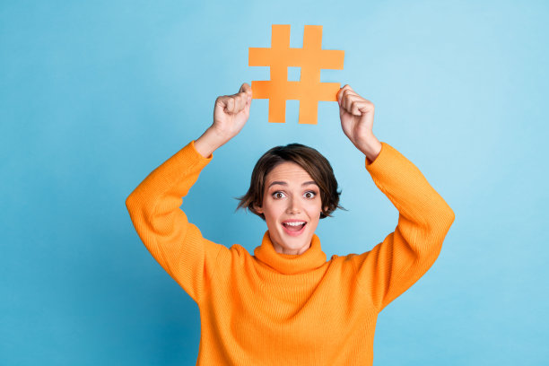 漂亮的年轻女孩的照片，举着标签，兴奋的网红穿着时髦的橙色衣服，在蓝色的背景上孤立起来图片下载