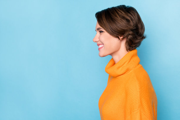 照片肖像的漂亮年轻的女孩侧面看起来牙齿灿烂的微笑穿着时尚的橙色衣服孤立的蓝色背景图片下载
