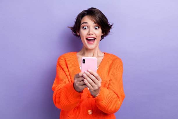 照片中，兴奋有趣的女人穿着橙色开襟羊毛衫写着苹果三星小工具孤立的紫罗兰色背景图片下载