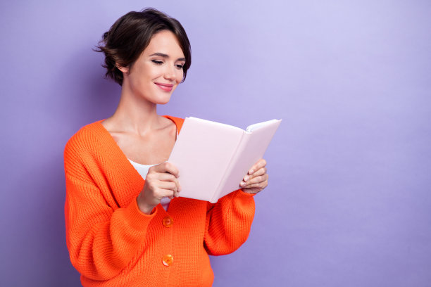 照片中的聪明快乐的女士穿着时髦的橙色衣服阅读新书的空白空间孤立在紫色的背景图片下载