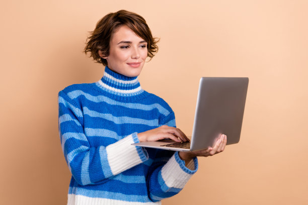 照片的自信漂亮的女人穿着毛衣工作的苹果三星现代设备孤立的米色背景图片下载