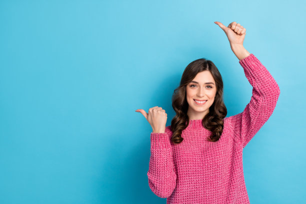 可爱开朗的女士穿着时髦衣服的照片，两只手臂在头顶上方，在蓝色的背景上把品质装空隔开图片下载