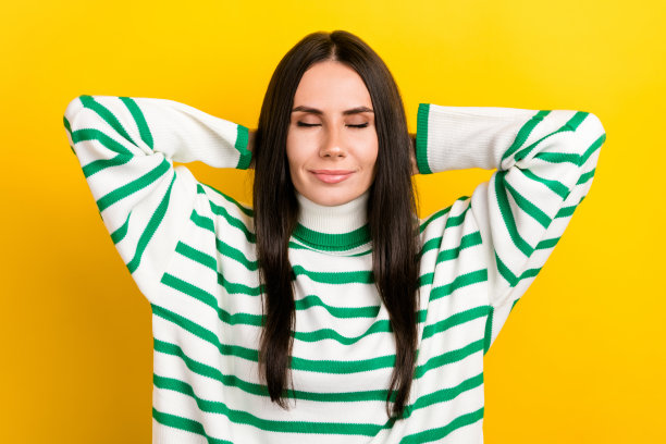 照片中，梦幻般的可爱女人穿着条纹毛衣，闭着眼睛，手臂在头后，孤立的黄色背景图片下载