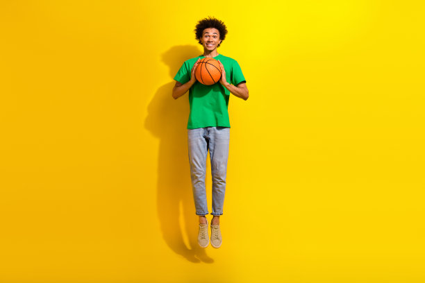 时髦酷的家伙穿着绿色t恤跳高上升球的全身照片，空旷的空间孤立的黄色背景图片下载