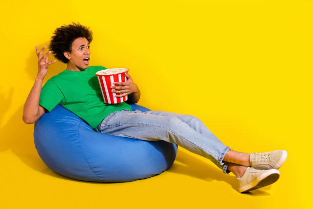 时髦印象深刻的家伙穿着绿色t恤看电影吃爆米花空的空间孤立的黄色背景的全长照片图片下载