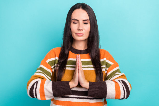 照片中甜美可爱的女子穿着条纹毛衣双臂合在一起享受瑜伽，闭上眼睛孤立的绿松石色背景图片下载