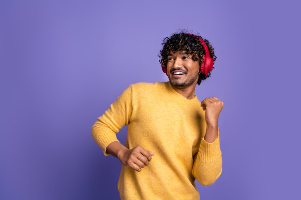 时髦积极的男人的照片，穿着时髦的黄色衣服，听音乐，现代科技孤立在紫色的背景图片下载