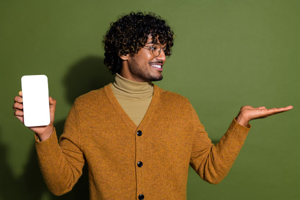 照片中，迷人的年轻人手持白色屏幕，看起来空无一人，穿着时髦的棕色衣服，孤立在卡其色背景上图片下载