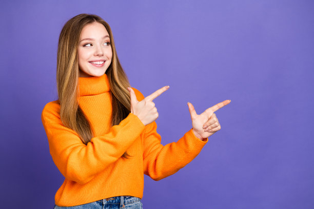 照片的青年金发可爱的快乐的微笑女孩在橙色高领毛衣指着手指宣布孤立的紫罗兰色背景图片下载