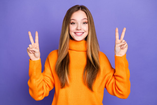 青春的肖像照片迷人的金发可爱的快乐的微笑女孩v标志趋势在橙色高领衫孤立的紫罗兰色背景图片下载