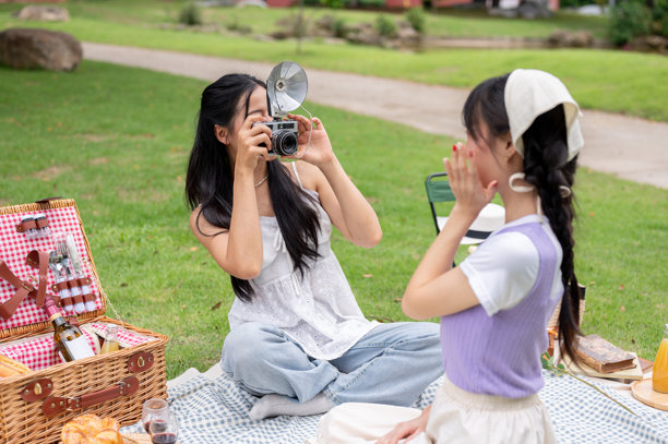一个快乐的亚洲女人用复古相机给她的朋友拍了一张野餐的照片。图片下载