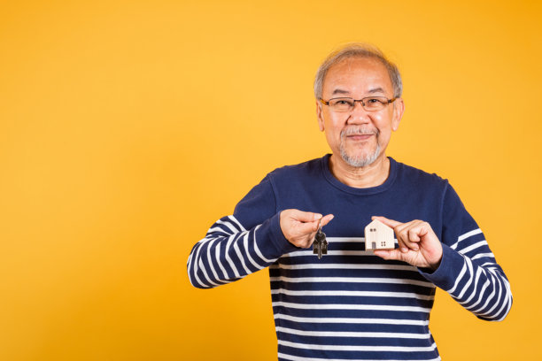 肖像亚洲面带微笑的老人戴着眼镜拿着钥匙和一个小房子模特工作室拍摄孤立的黄色背景图片下载