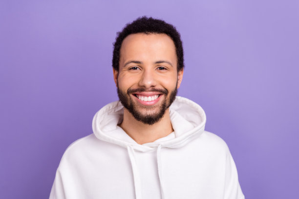 照片的好心情开朗积极的男子与卷曲的发型穿着白色卫衣微笑牙科广告孤立的紫色背景图片下载