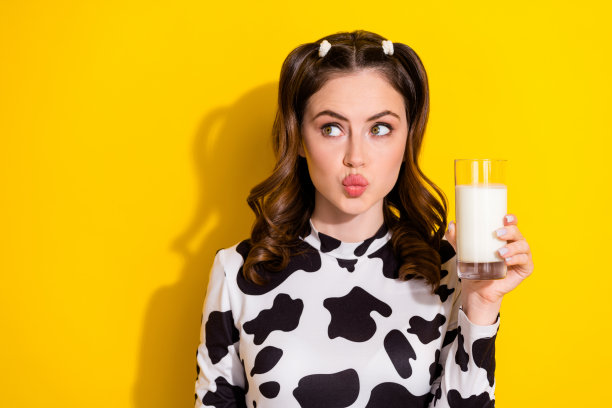 照片中，兴奋的漂亮女孩卷着一头卷发，穿着奶牛长袖，拿着牛奶，在黄色的背景上看起来空无一物图片下载