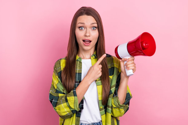 印象深刻的惊讶女人的照片，长发型，格子衬衫，盯着粉红色背景上孤立的扬声器图片下载