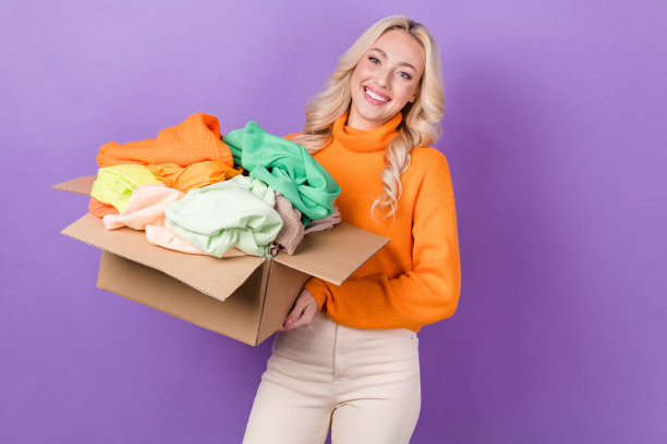 照片相当积极的女士手拿纸板箱衣服的东西孤立的紫色背景图片下载
