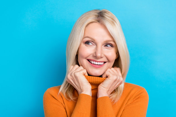 高级妇女触摸领高领毛衣的特写照片，微笑着看空空间，梦想着她的孩子们被隔离在海蓝宝石的背景上图片下载