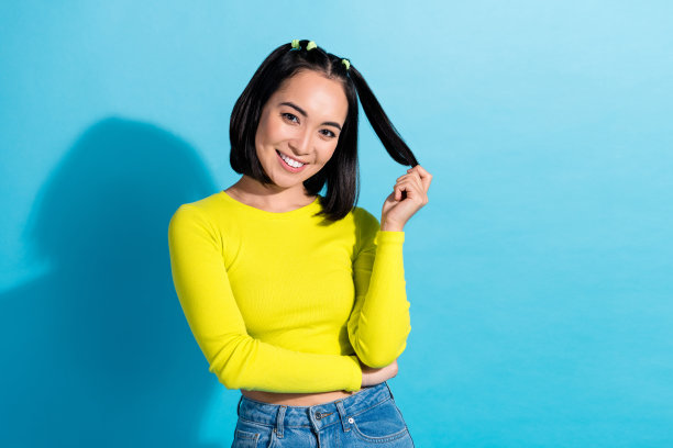 可爱开朗的漂亮女孩的肖像照片漂亮的韩国女人玩发型尾巴穿时髦的黄色上衣孤立的蓝色背景图片下载