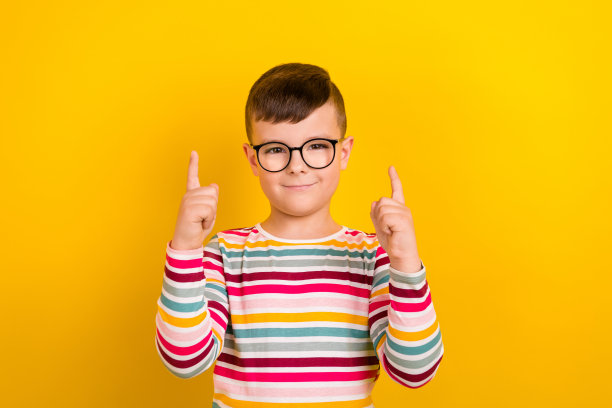 照片中开朗可爱的男孩戴着眼镜，两只手臂上有条纹的时髦衣服，在黄色的背景上显示出空旷的空间图片下载