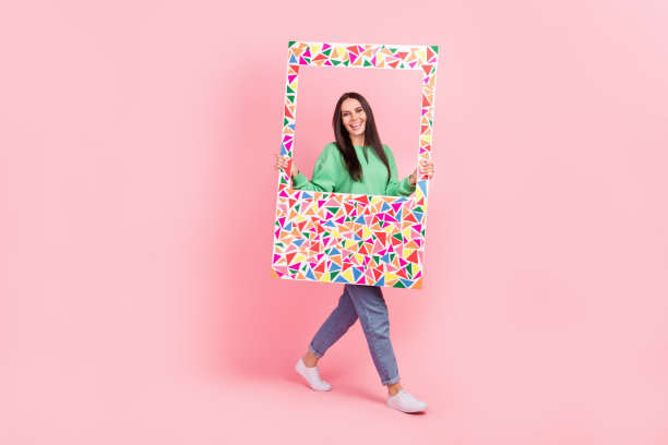 可爱的正面女士的全身照片，穿着亮绿色的衣服，拿着大纸，在粉红色的背景上移动空白的空间图片下载