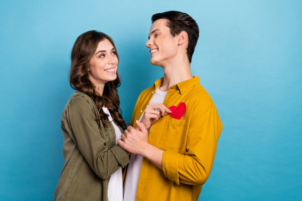 照片中的年轻夫妇积极满意拥抱庆祝结婚蜜月，纸红色心形孤立在蓝色的背景图片下载
