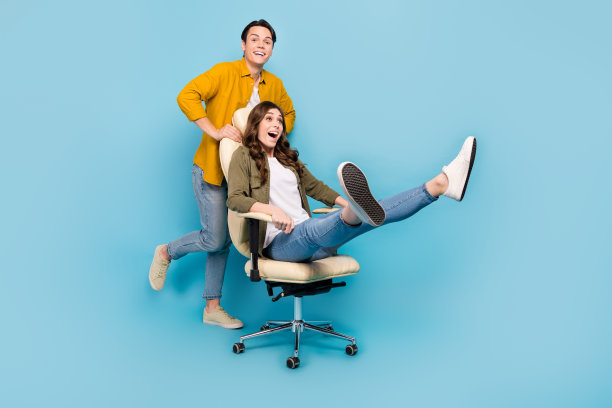 在蓝色的背景上，全身照片滑稽的大喜过望玩情侣推老板椅子舒适活动快速度移动孤立图片下载