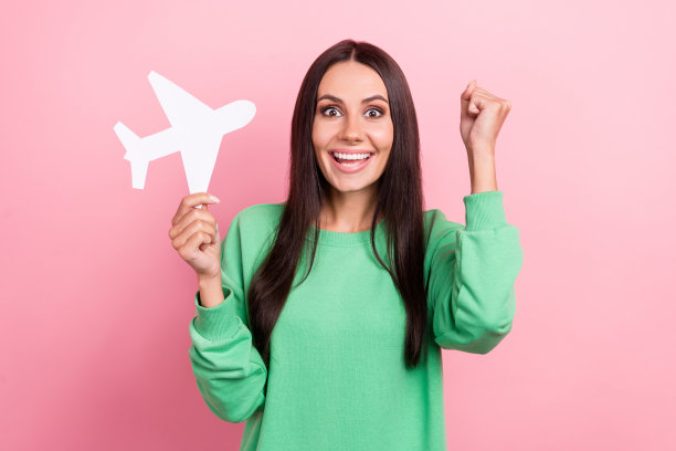 照片欣喜若狂的推动者年轻女孩黑发举起拳头拿纸飞机赢得免费假期周末孤立在粉红色的背景图片下载