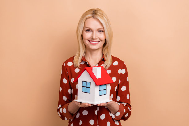友好积极的女士的照片，露齿微笑手臂抱显示小房子孤立的米色背景图片下载