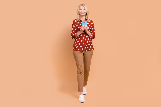 正面漂亮女士的全身照片，用电话走路，牙齿微笑，孤立在米色背景上图片下载