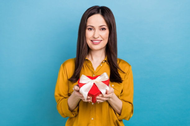 照片中漂亮可爱的女士穿着黄色衬衫，展示红色巧克力糖果盒，背景是蓝色的图片下载