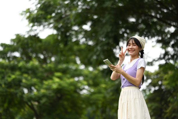 一个快乐的年轻亚洲女人在公园里用手机的照片图片下载