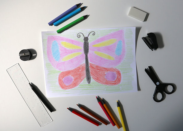 一个孩子用彩色铅笔画画的照片。画一只蝴蝶。办公设备就在附近。白色背景。图片下载