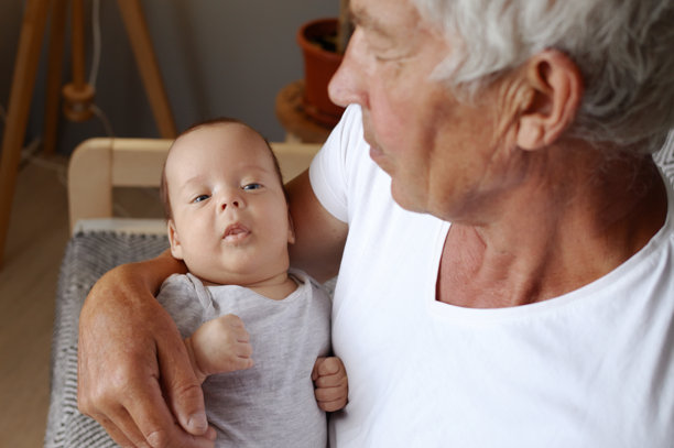 祖父怀里平静的婴儿。穿着白t恤的退休老人在家里抱着刚出生的孩子图片下载