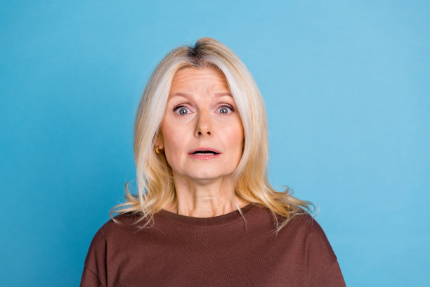 照片中，焦虑、紧张、可爱的老年妇女穿着时髦的棕色衣服，孤立在蓝色的背景上图片下载