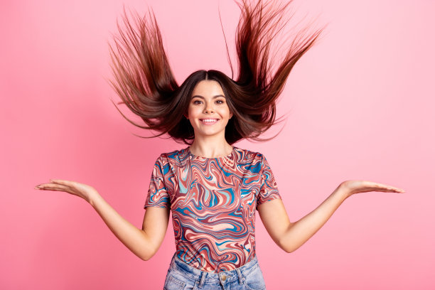 照片中迷人甜美的女孩穿着印花t恤，头发飞扬，对比双臂空白，孤立的粉红色背景图片下载