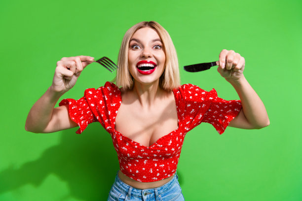 照片中兴奋的女孩用刀叉吃食物孤立的绿色背景图片下载
