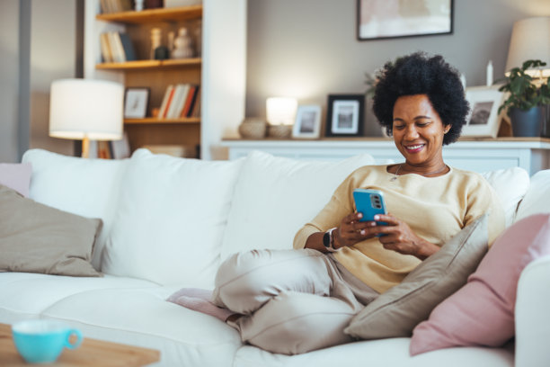 一个漂亮的年轻女子白天在客厅用手机的剪辑照片。图片下载