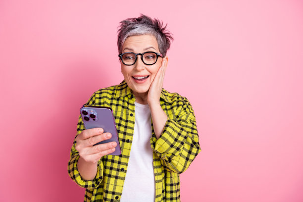 漂亮的老年妇女的照片使用手机空的空间格子衬衫孤立的粉红色背景图片下载