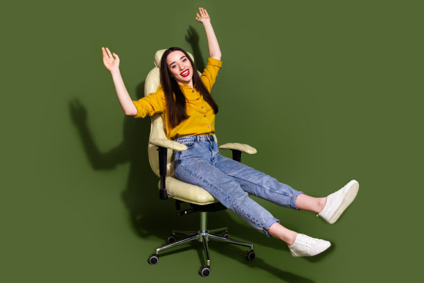 开朗悠闲的女士穿着黄色衬衫坐在办公椅空空间孤立的卡其色背景的全长照片图片下载
