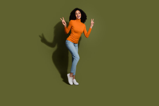 迷人的正面女性穿着橙色毛衣的全长照片，显示两个v字空白空间孤立的卡其色背景图片下载