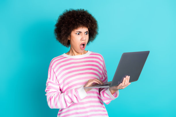 漂亮的年轻女子使用笔记本电脑，穿套头衫孤立的蓝绿色背景的照片图片下载